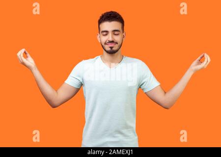 Üben Sie Achtsamkeit. Portrait eines ruhigen, stattlichen brünetten Mannes mit Bart in weißem T-Shirt, der mit den Fingern Meditationsgeste macht und Stress bewältigung. I Stockfoto