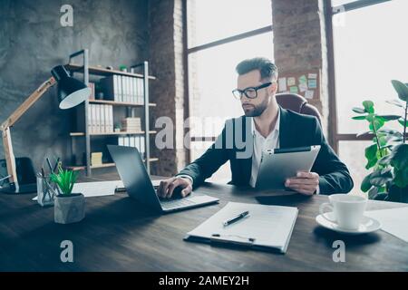 Foto des gutaussehenden Geschäftschefs, der E-Reader hält, um den Notebook-Bericht zu überprüfen, in dem Partner und eigene Finanznummern verglichen werden, trägt den schwarzen Blazer Stockfoto