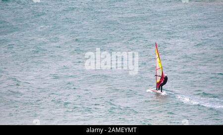 Ein Panoramabild eines Windsurfers, der mit Geschwindigkeit auf dem Meer bei Crantock in Newquay in Cornwall gleitete. Stockfoto