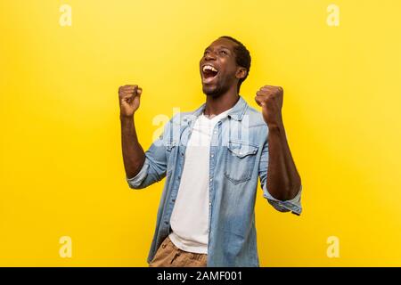 Porträt eines ekstatischen überfröhlichen, gutaussehenden Mannes in Jeans-Casual-Hemd, das mit erhobenen Fäusten und Schreien die siegreiche Geste ausdrückt und den Sieg feiert. IND Stockfoto