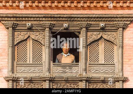 Alter Mann in einem Fenster mit Holzschnitzereien in Kathmandu, Nepal Stockfoto