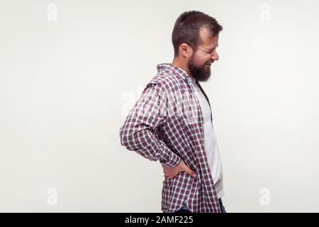 Portrait eines ungesunden bärtigen Mannes in legeren Pairshirt, das Wunden Rücken berührt, Rückenschmerzen spürt, den eingeklemmten Nerv schmerzt die untere Wirbelsäule, Nierenentzündung. In Stockfoto