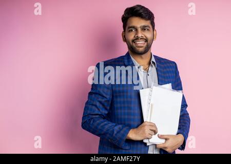 Innenschuss von einem glücklichen erfolgreichen Mann, einem Finanzier, einem Manager, gekleidet mit formeller Kleidung, mit Dokumentation, Finanzbericht, Papieren, lächelnder Stellung a Stockfoto