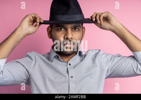 Studioporträt von gutaussehenden jungen indischen Männern mit kleinem Bart, grauem Hemd und schwarzem Hut, Kamera mit ernsthaftem Ausdruck, posierend OV Stockfoto