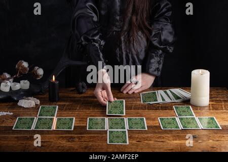 Frau erzählt die Zukunft mit Spielkarten. Tarot-Kartenkonzept auf dem Tisch. Vorhersage der Zukunft. Die Hände des Fortunetellers in schwarzem Gewand. Stockfoto