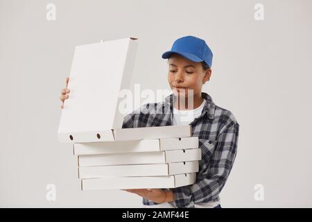 Taille hoch Portrait der schönen jungen Frau, die Pizzakisten hält und nach innen schaut, während sie für fast Food arbeitet und vor weißem Hintergrund steht, Platz für Kopien Stockfoto