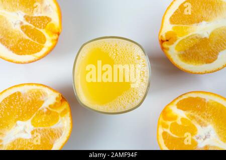 Frisch gepresster Orangensaft in einem Glas auf einem Tisch mit Orangenscheiben daneben. Erfrischendes gelbes Getränk mit Früchten auf weißem Hintergrund Stockfoto