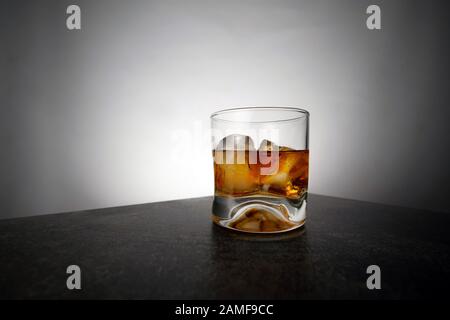 Glas goldener Whisky im Alter mit Eiswürfeln auf dem Tisch. Orangefarbenes Alkoholgetränk mit Felsen an der Bar Stockfoto