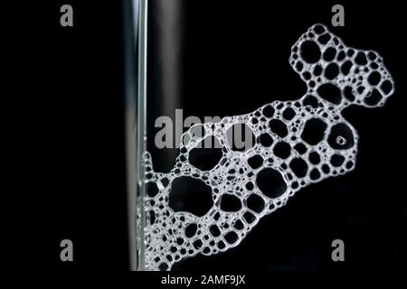 Nahaufnahme des Vaterschaums auf Glas auf schwarzem Hintergrund. Makroaufnahme von Biertrinkschaum auf transparentem Glas Stockfoto