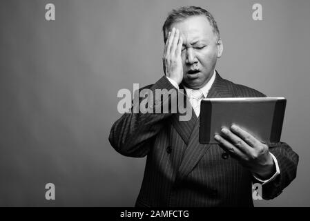 Studio mit Digitaltablett vor grauem Hintergrund in Schwarzweiß von reifen asiatischen Geschäftsleuten aufgenommen Stockfoto