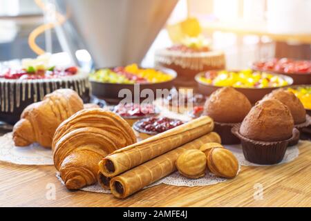 Produktion für die Herstellung von Desserts. Croissants und Kuchen in Tortlets mit Kuchen, Nüsse mit Kondensmilch liegen auf einem Holztisch. Stockfoto