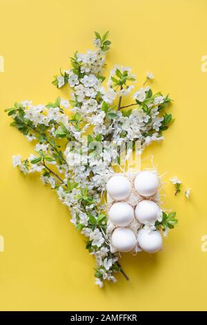 Frühlingskomposition von Hühnereiern mit frischen Blumen in Porzellanbox auf Gelb. Ostern. Vertikal. Ansicht von oben. Stockfoto
