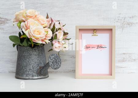 Verspottet Stillleben Bilderrahmen und an der Gießkanne mit Rosenstrauß auf grunztem weißem Holz. Valentines Tag Hintergrundkonzept. Verspotten Sie sich mit Foto Stockfoto