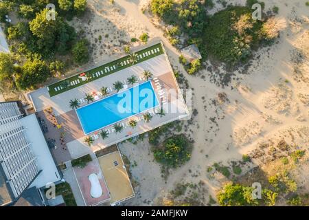 Von oben nach unten Luftbild von Hotel Schwimmbad mit kristallklarem Wasser mit Palmen und Liegestühlen mit Stühlen in der Resort City in der Nähe des Meeres in w umgeben Stockfoto