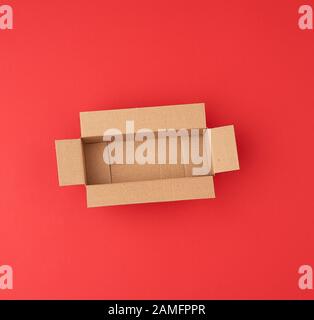 Öffnen Sie die leere, quadratische, braune Kartonschachtel für Transport und Verpackung von Waren auf rotem Hintergrund, Draufsicht. Stockfoto