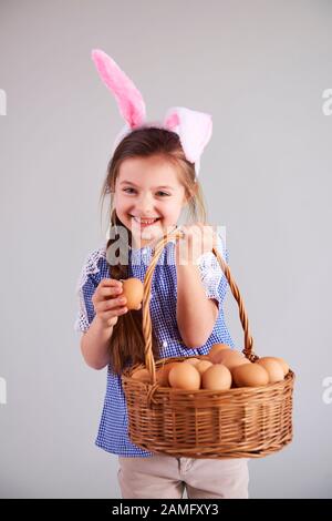 Lächelnde Frau in Kaninchen-Kostüm, die einen Korb mit Eiern hält Stockfoto