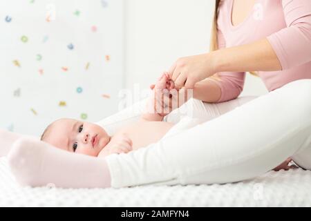 Hintergrund der Babymassage. Mutter massiert ihren kleinen Jungen sanft. Baby, das auf dem Rücken liegt und während der Massage auf die Kamera blickt. Stockfoto