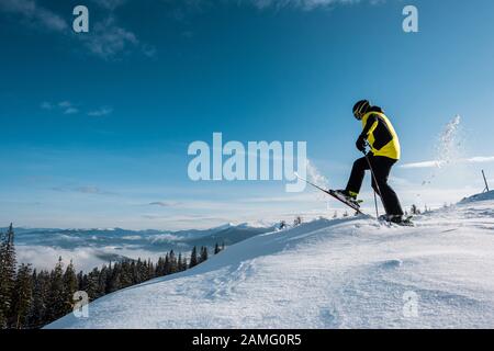 Seitenansicht des Skifahrers, der Skistöcke hält und in den Bergen gegen den Himmel tritt Stockfoto