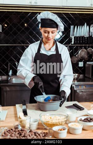 Fröhlicher Chocolatier, der Silikonspachtel hält, während er Schokolade in der Schüssel mischt Stockfoto