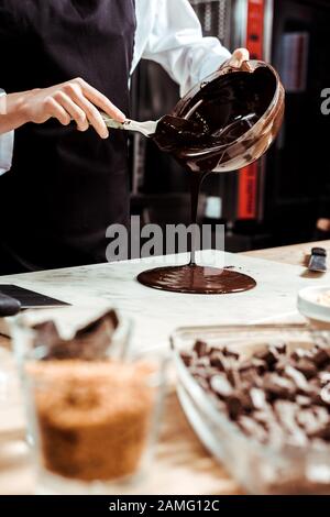Selektiver Fokus des Chocolatiers, der geschmolzene Schokolade auf die Marmoroberfläche gießt Stockfoto
