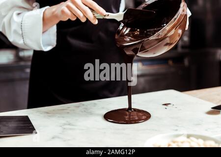 3/4-Blick auf Chocolatier, der geschmolzene Schokolade auf die Marmoroberfläche gießt Stockfoto