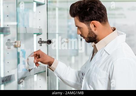 Seitenansicht des Apothekers, der Pillen aus dem Vorzeigeboden nimmt Stockfoto