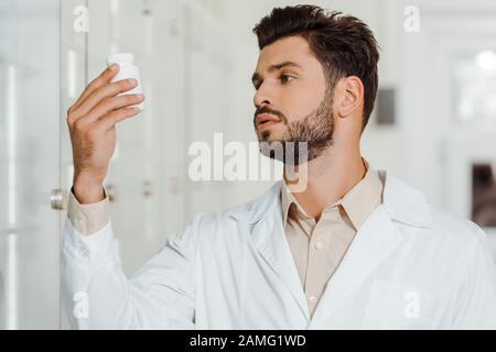 Drogist in weißem Mantel mit Blick auf den Mixbecher mit Pillen in der Apotheke Stockfoto