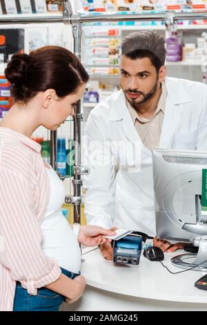 Pharmazeutin sucht schwangere Frau, die mit paypass in Drogerie bezahlt Stockfoto