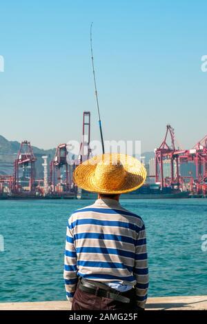 Fisher Mann mit Angelrute von hinten in der Nähe der Container schiff und Fracht Hafen in HongKong Stockfoto