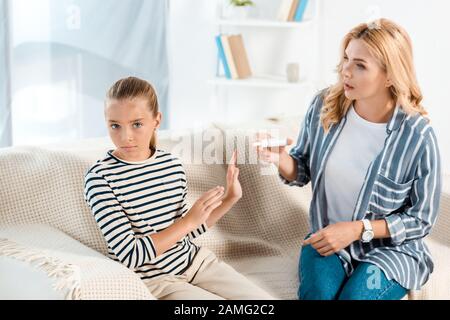 Krankes Kind, das in der Nähe der Mutter gestikuliert wurde, die Nasenspray im Wohnzimmer hält Stockfoto