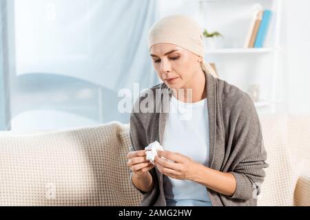 Kranke Frau mit Kopftuch, die Gewebe hält, während sie auf dem Sofa sitzt Stockfoto