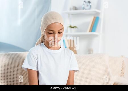 Frustriertes Kind im Kopftuch, das auf dem Sofa im Wohnzimmer sitzt Stockfoto