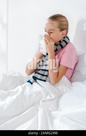 Krankes Kind mit geschlossenen Augen, das in Gewebe niest Stockfoto