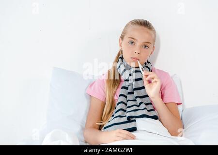 Krankes Kind mit digitalem Thermometer im Mund, das auf die Kamera blickt Stockfoto
