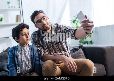 Lächelnder jüdischer Vater nimmt selfie mit niedlichem Sohn in Wohnung Stockfoto