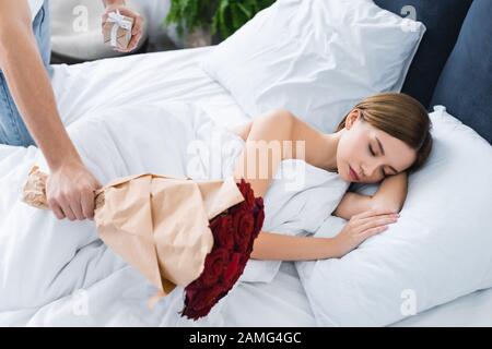 3/4-Ansicht des Mannes, der Geschenk, Blumenstrauß und Frau im Bett hält Stockfoto