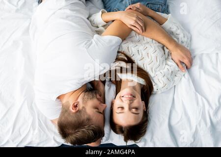 Draufsicht auf gutaussehenden Mann, der eine attraktive und lächelnde Frau in der Wohnung umarmt Stockfoto