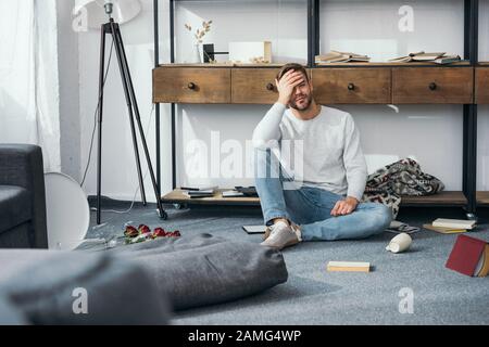 Gutaussehender und schockierter Mann, der Gesicht in der geraubten Wohnung verdeckte Stockfoto