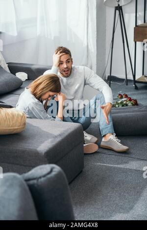 Traurige Frau und schockierter Mann, der auf dem Boden in einer geraubten Wohnung sitzt Stockfoto