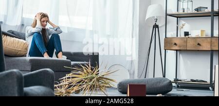 Panoramaschuss von attraktiver und trauriger Frau, die auf dem Sofa in einer geraubten Wohnung sitzt Stockfoto