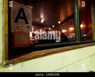 Blick auf das Bar-Interieur von der Straße, mit Hinweisplatte für die Sanitäre Inspektion "A" in Window, New York City, New York, 25. März 2019. () Stockfoto