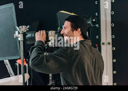 Seitenansicht des lächelnden, gutaussehenden Kameramanns, der im Fotostudio arbeitet Stockfoto