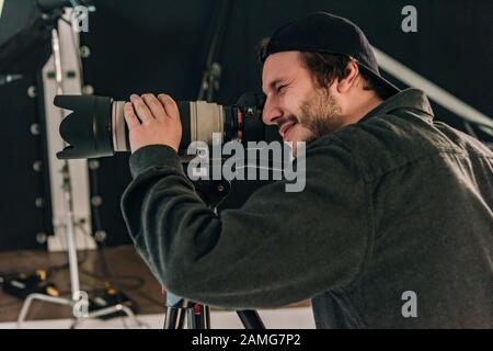 Seitenansicht des lächelnden Kameramanns mit Kamera am Arbeitsplatz Stockfoto