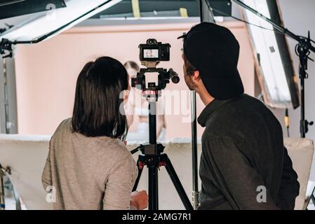 Rückansicht von Kameramann und Assistent, die während der Arbeit mit Frau im Fotostudio auf das Kameradisplay blicken Stockfoto