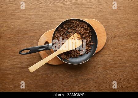 Draufsicht über Hackfleisch in Bratpfanne auf Hackbrett auf Holzhintergrund Stockfoto