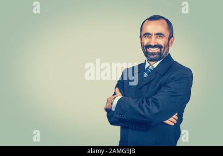 Bärtiger Mann mit Krawatte, blaues Hemd mit roter Krawatte. Gekreuzte Arme. Ein lächelnder Arbeitgeber, der Sie auf eine Kamera blickt, isoliert auf hellgrün-gelbem Hintergrund. P Stockfoto