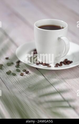 Eine Tasse heißen Kaffee mit gebratenen Kaffeebohnen auf weißem Holztisch. Stockfoto