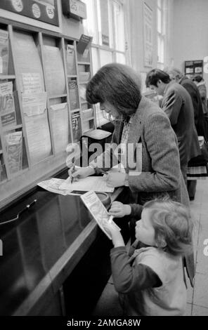 Post Office 1980s London UK. Personen, die Formulare ausfüllen, indem sie Broschüren auswählen. Mutter und Kind, die 1981 ZU HOMER SYKES in die Post gingen Stockfoto