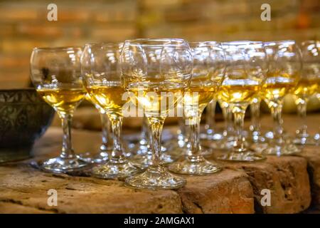 Reihen transparenter Glasgläser für Wein, der mit Bernsteinwein auf einer Steinoberfläche gefüllt ist Stockfoto