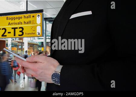Nahaufnahme eines Geschäftsmannes in einem schwarzen Anzug, der ein Smartphone in einem Flughafen hält Stockfoto